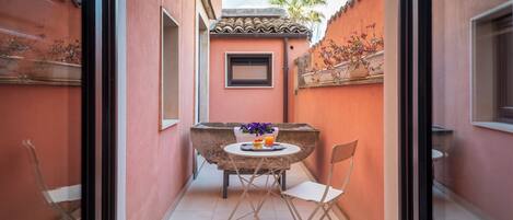 Un pequeño patio al aire libre con una mesa, sillas, un ventanal y una planta en maceta.