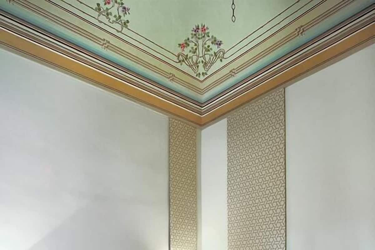A hotel room with a bed, nightstands, a desk, and a patterned wall.