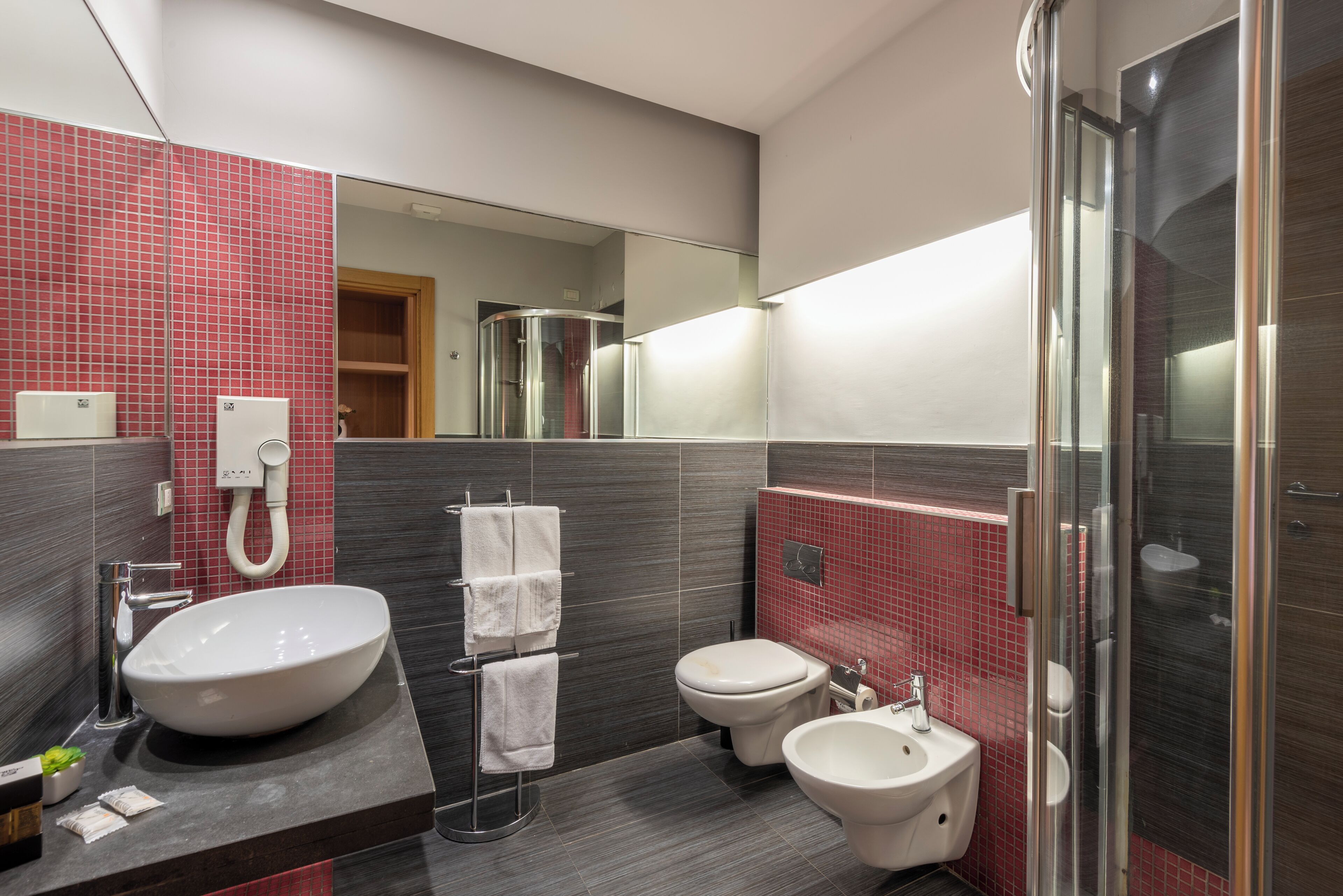 A modern bathroom with a large sink, toilet, bidet, and a glass shower enclosure.