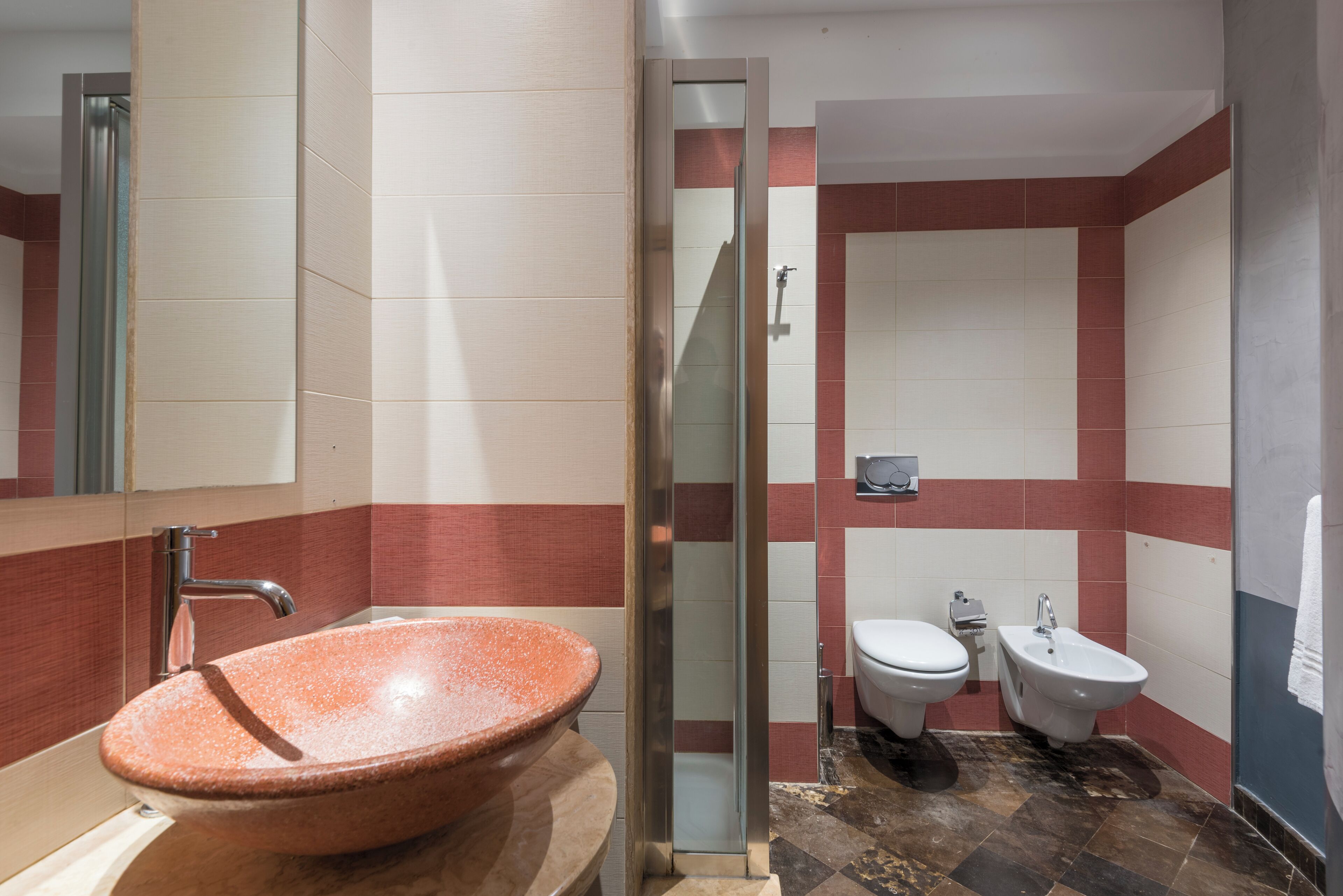 A bathroom with a large oval sink, a glass-enclosed shower, a toilet, and a bidet.