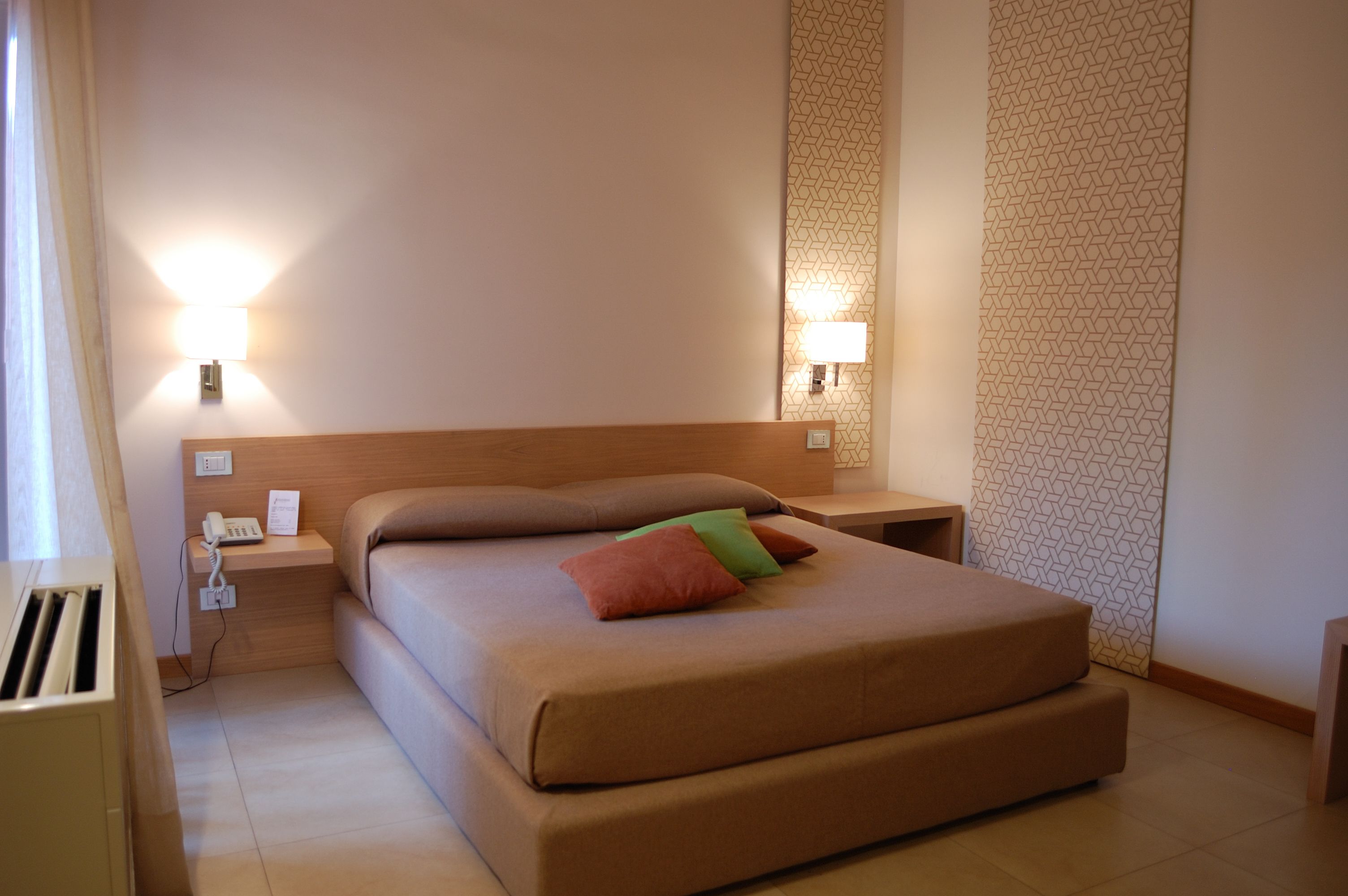 A hotel room with a large bed, two bedside lamps, a bedside telephone, and a patterned wall.