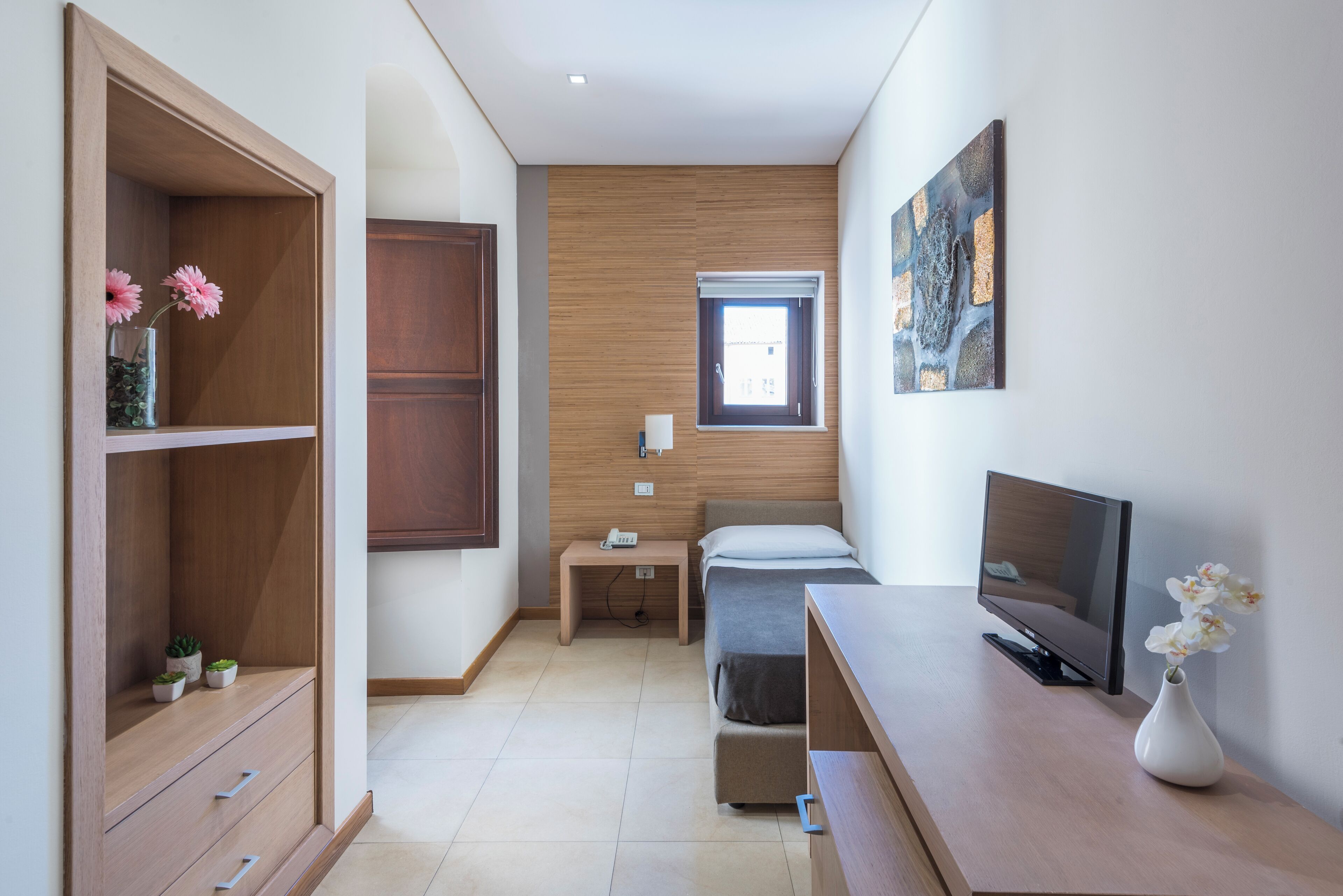A compact bedroom with a bed, bedside table, TV, and a small window.