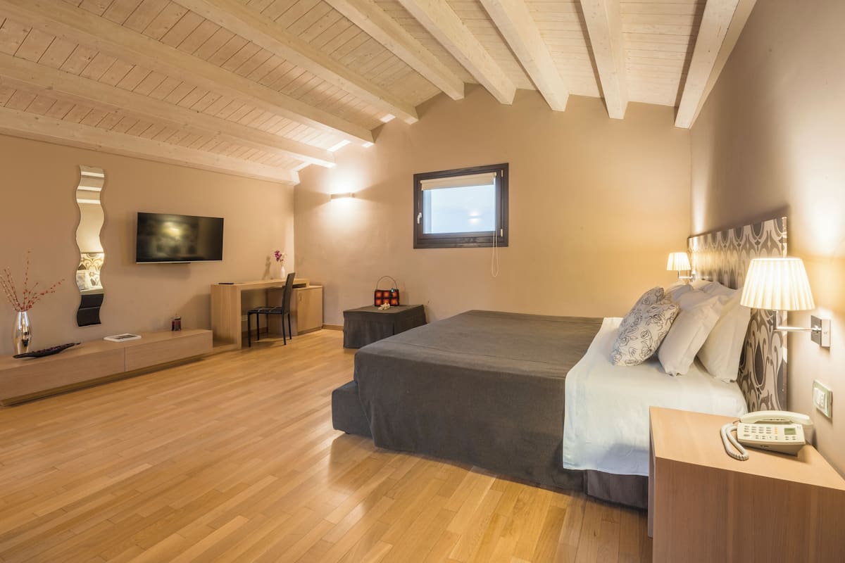 A modern hotel room with a large bed, a desk, a TV, and a window.