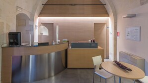 A reception area with a modern design, featuring a reception desk, a computer, a glass partition, and a seating area with a table and chairs.