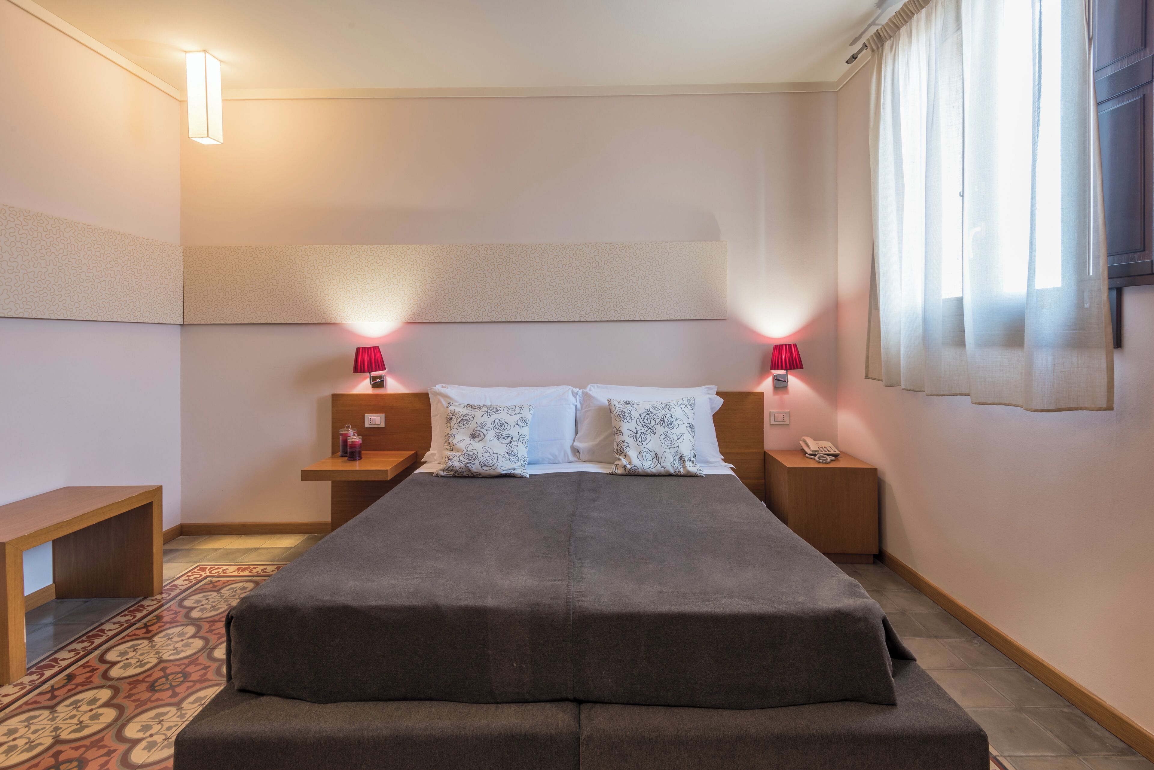 Una habitación de hotel moderna con una cama grande, mesitas de noche con lámparas, una mesita auxiliar de madera y una alfombra estampada.