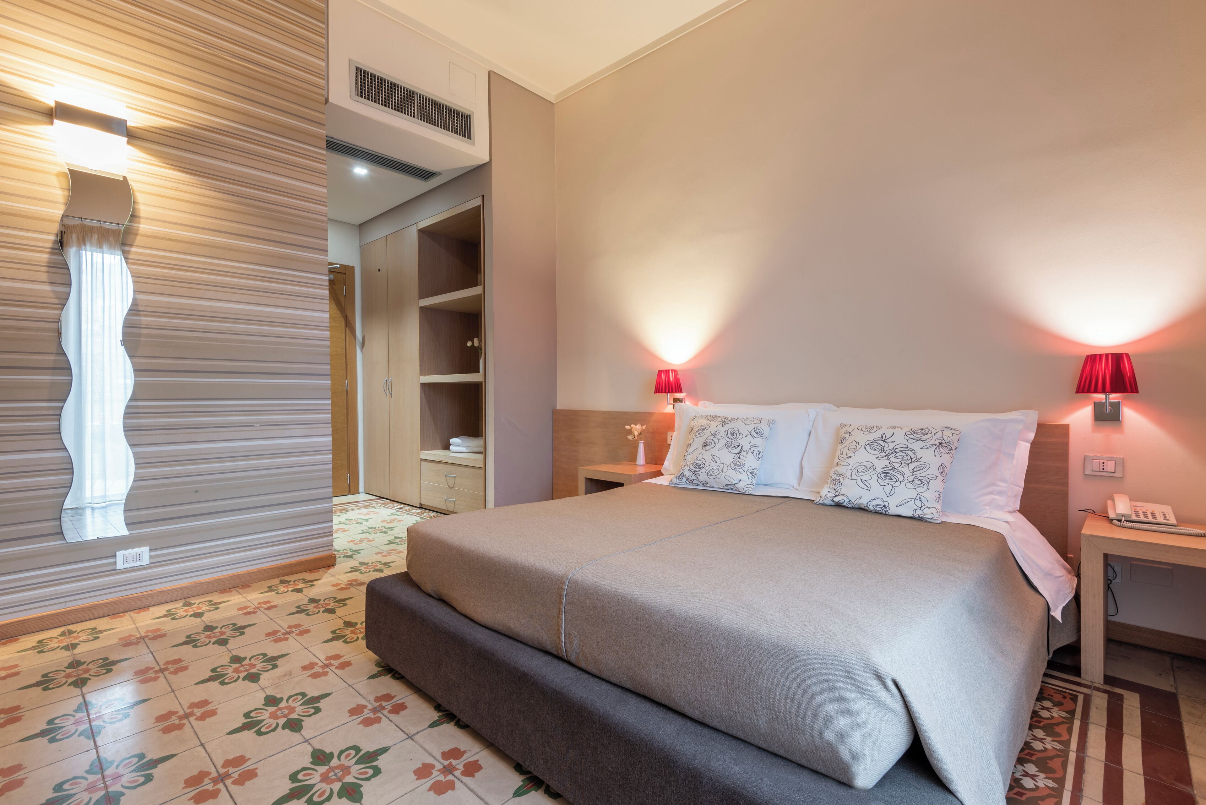 Un dormitorio con cama, mesitas de noche, armario y lámpara de pared.