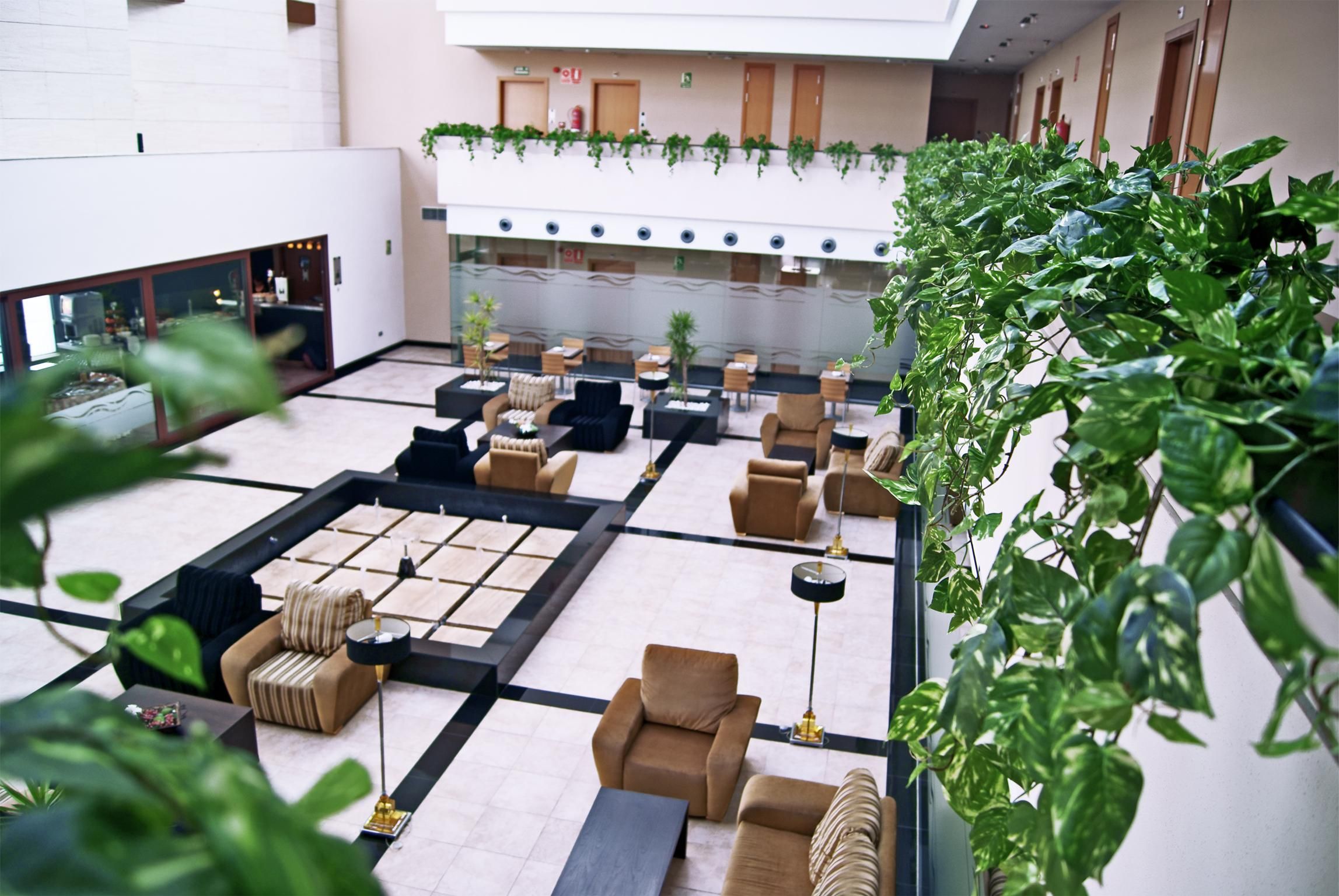 A spacious lobby with multiple seating areas, a central water feature, and a balcony with greenery.