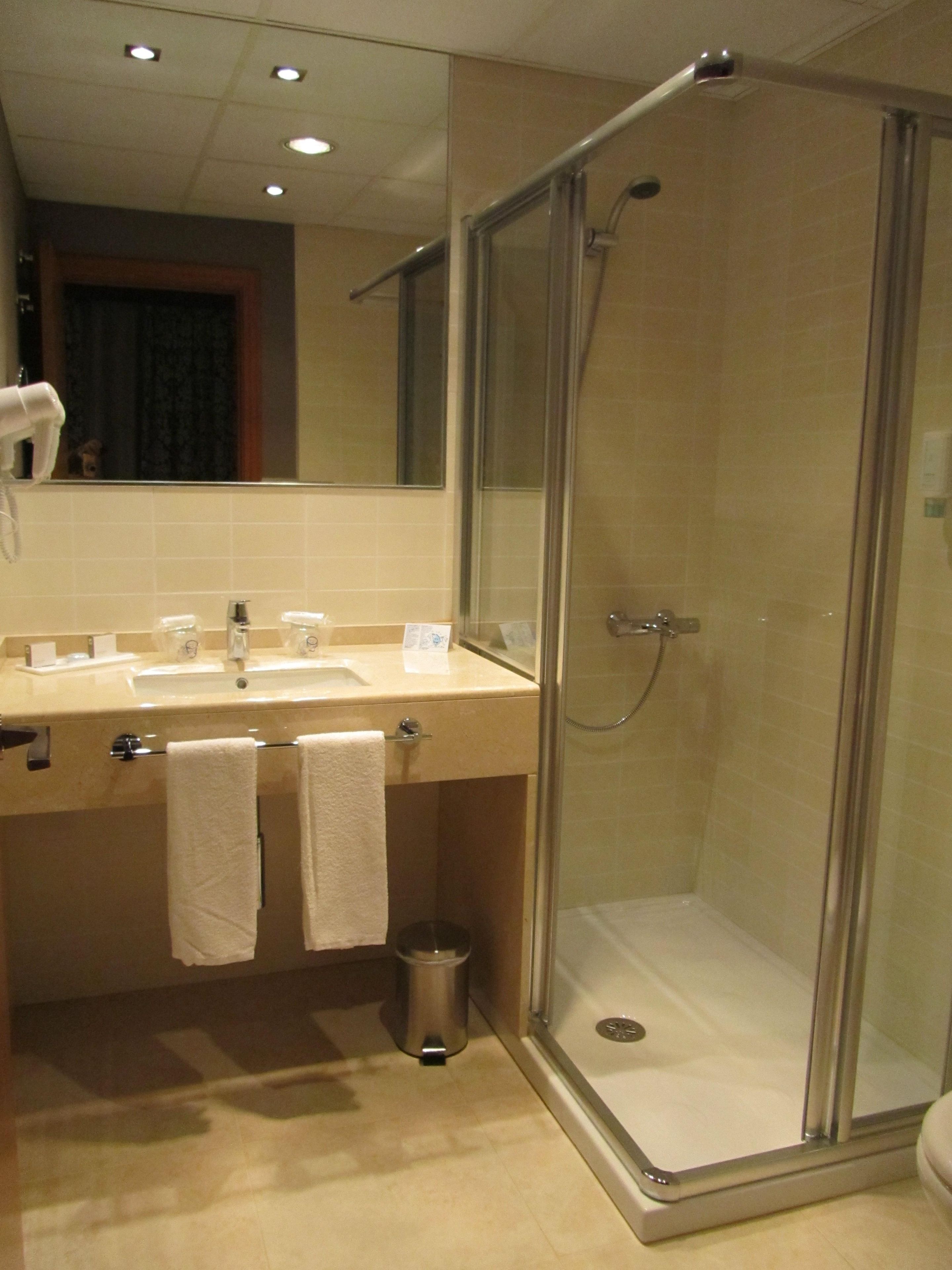A modern bathroom with a glass-enclosed shower, a sink with a mirror, and two towels hanging on the wall.
