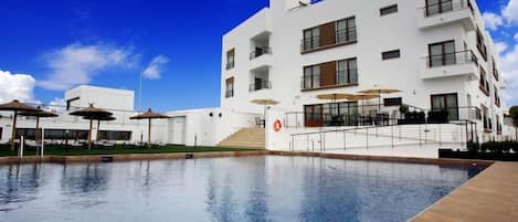 Una piscina al aire libre, sombrillas, sillones reclinables de piscina