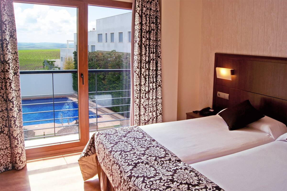 Quarto de hotel com cama grande, vista para uma piscina e varanda.