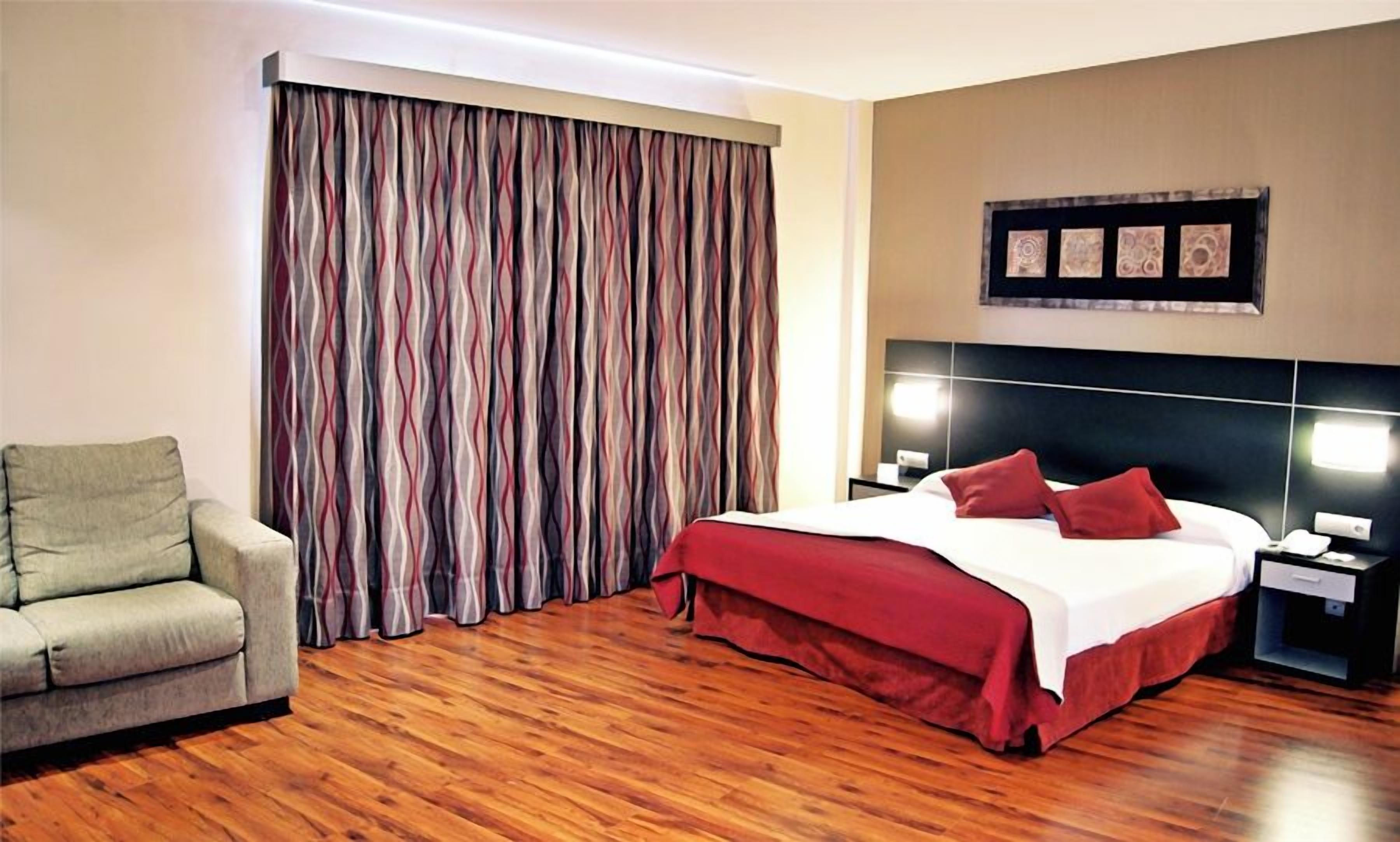 A hotel room with a bed, a chair, a nightstand, and a curtain.