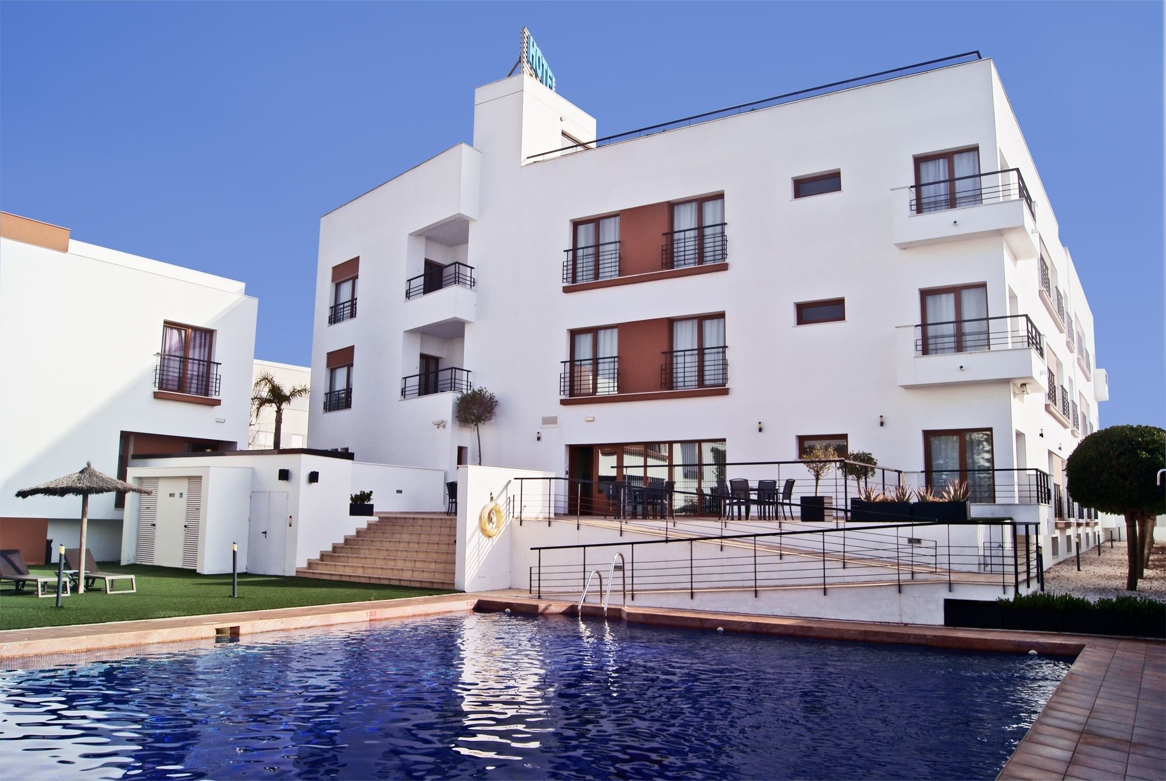 A modern hotel with a swimming pool, outdoor seating, and a well-maintained garden.