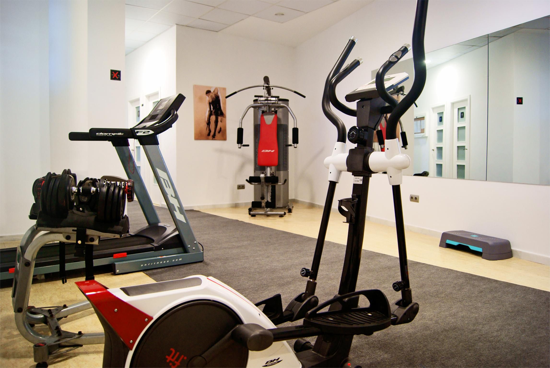A gym with cardio equipment, weight machines, and a mirror reflecting the room.