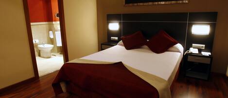 A hotel room with a large bed, two bedside tables, a nightstand, a mirror, and a bathroom visible through an open door.