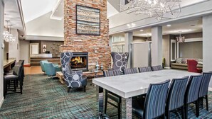 A modern hotel lobby with a fireplace, seating area, and a large dining table. - Residence Inn by Marriott San Antonio SeaWorld/Lackland (San Antonio)
