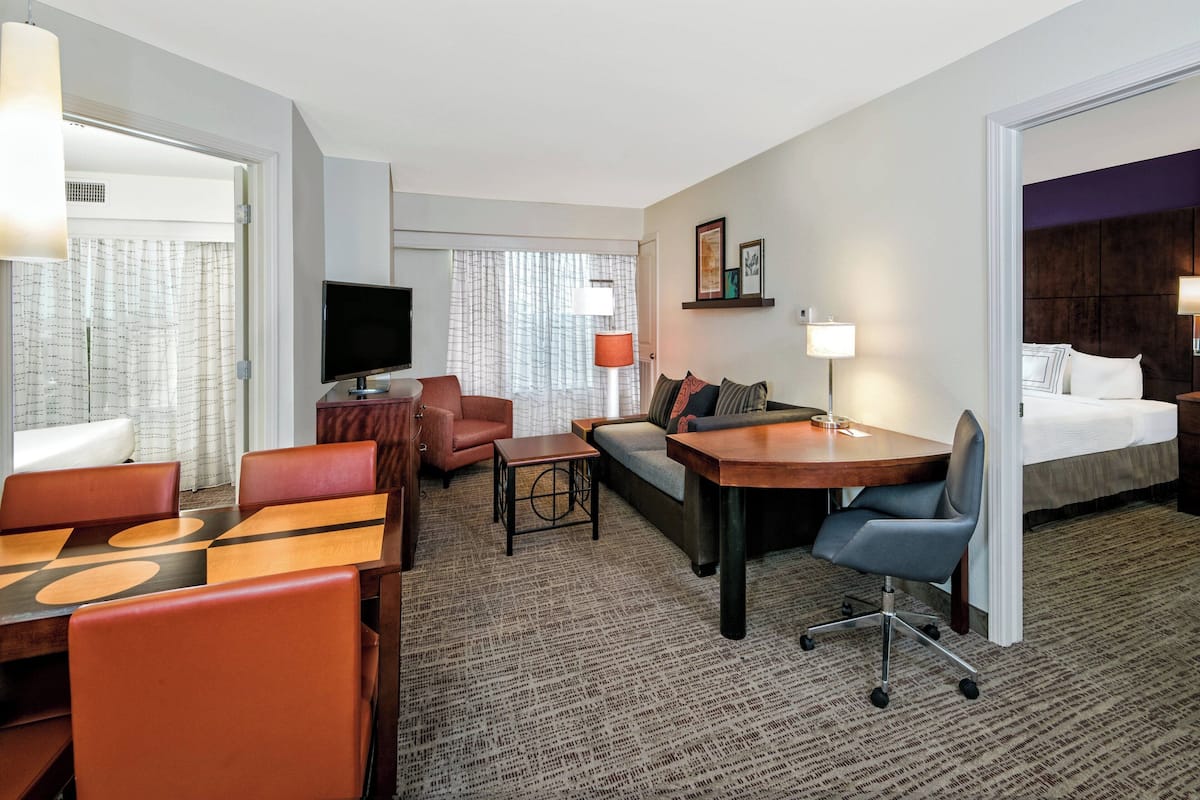 A hotel room with a dining area, a sofa, a bed, a TV, and a desk.