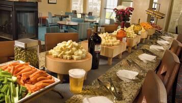 Una mesa de buffet con varios quesos, verduras y una botella de vino.