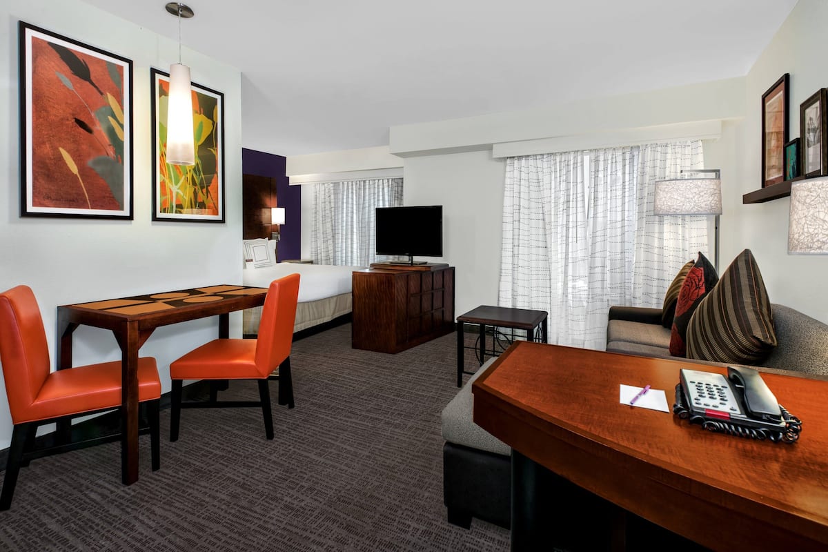 A hotel room with a dining area, a sofa, a TV, and artwork on the walls.