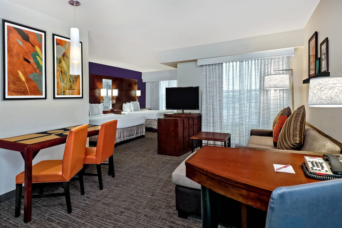 A hotel room with a dining area, a sofa, a TV, and artwork on the walls.