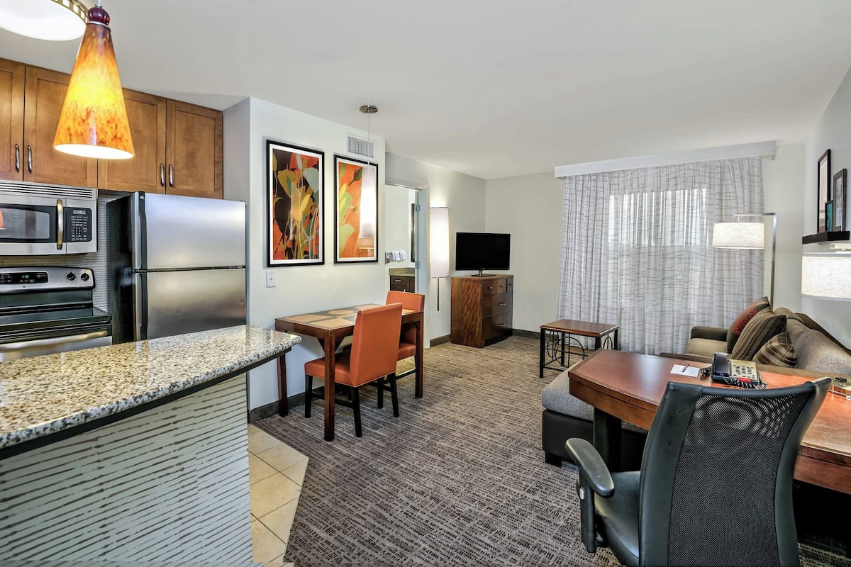 A modern hotel room with a kitchenette, dining area, and a living space.