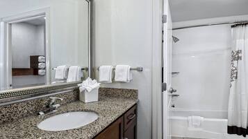 A bathroom with a granite countertop sink, a mirror, and a shower with a curtain.