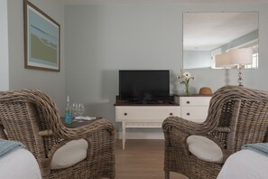 A room with two wicker chairs, a television on a white dresser, a mirror, and a lamp. - Chatham Seafarer Inn (Chatham)