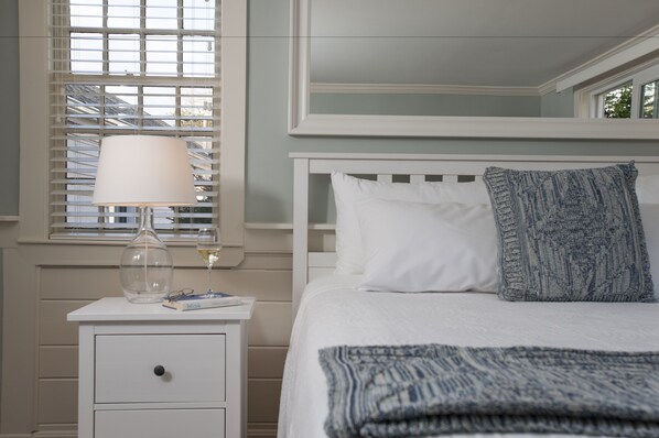 Un dormitorio ordenado con cama, mesita de noche con lámpara y ventana con persianas.