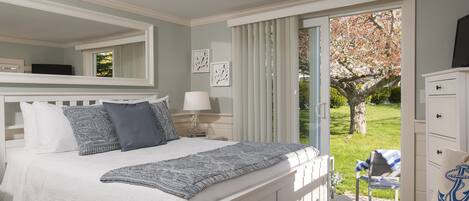 A bedroom with a bed, a nightstand, a lamp, a dresser, and a view of the outdoors.