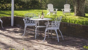 An outdoor patio with white metal chairs and a table, surrounded by blooming pink trees.