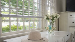A white desk with a woven hat, a vase with white flowers, and two glasses of white wine.