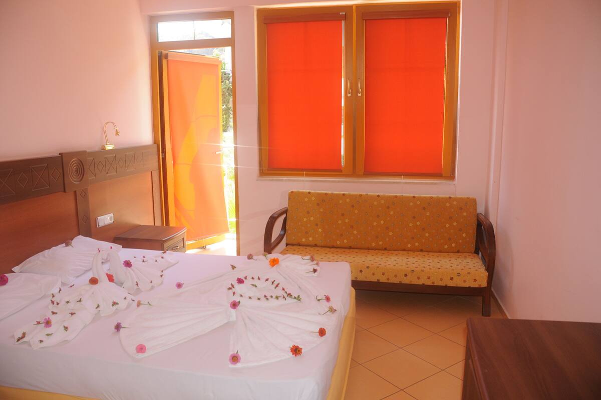 A hotel room with a bed, a sofa, and a window with orange blinds.