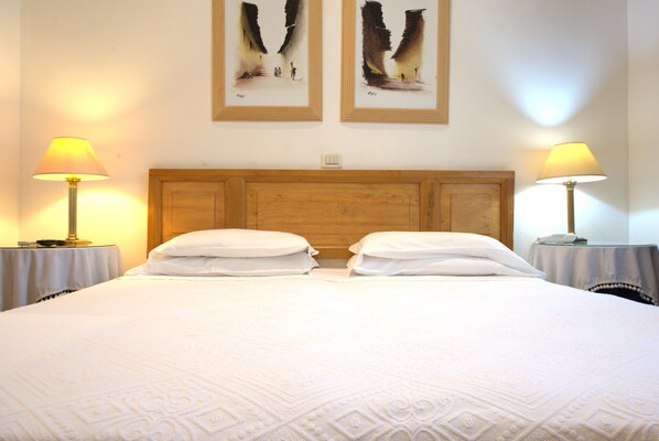 A double bed with a wooden headboard, two bedside lamps, and two framed artworks on the wall. - Hotel Locanda Cairoli (Rome)