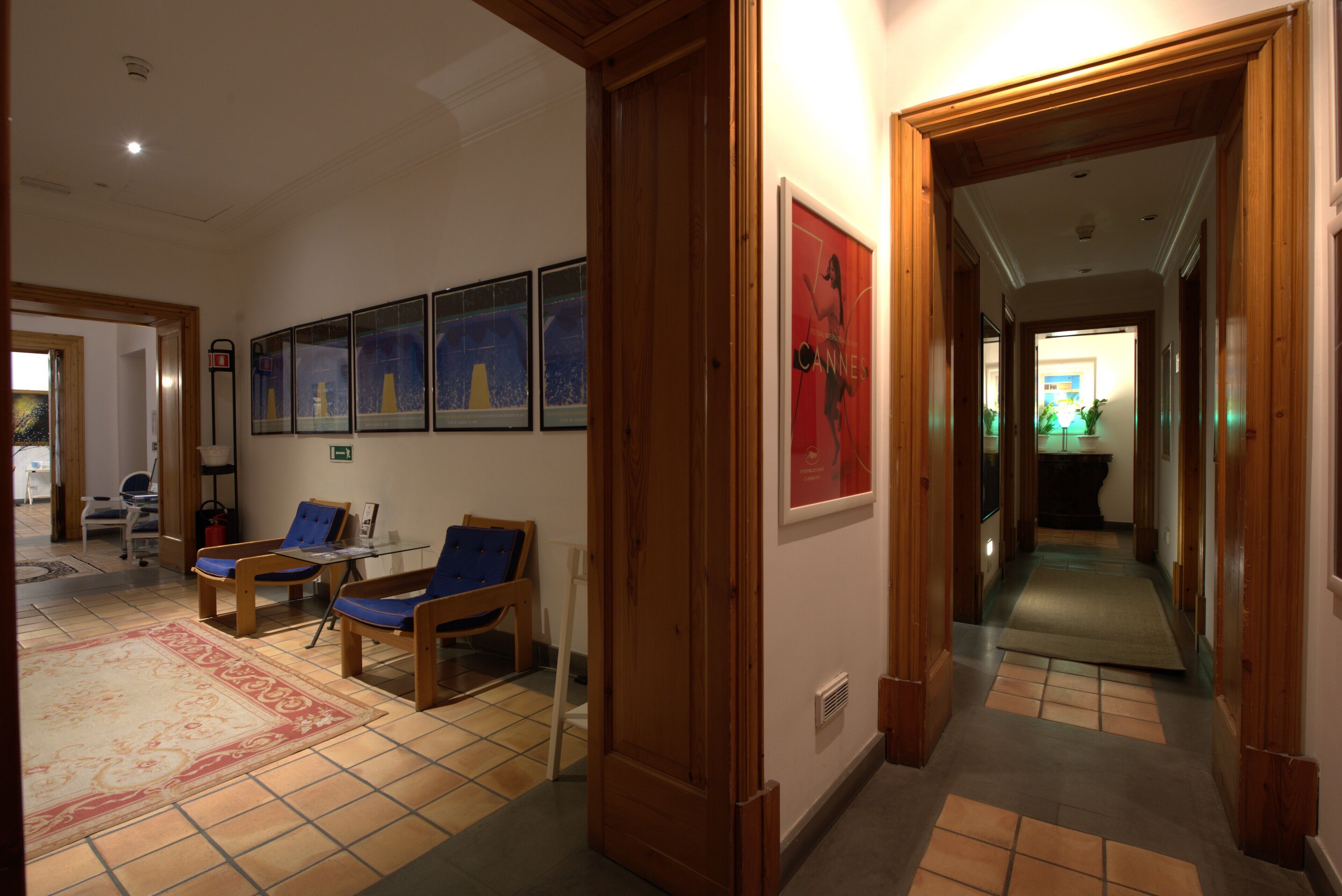 A hallway with wooden doors, a seating area with chairs, and framed artwork on the walls.
