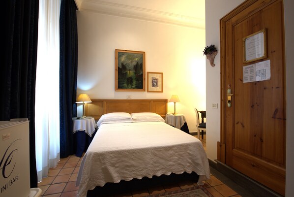 A hotel room with a bed, two bedside tables with lamps, a wooden door, and a wall-mounted painting. - Hotel Locanda Cairoli (Rome)