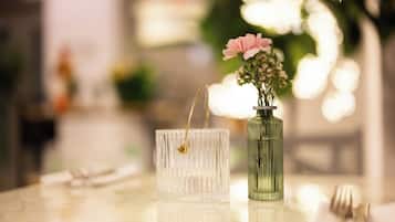 Una mesa con un florero de vidrio transparente con flores rosadas y un florero de vidrio verde con asa dorada.