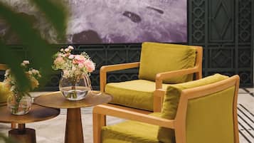 Quarto moderno com uma grande pintura abstrata, uma poltrona de madeira, uma pequena mesa redonda com um vaso de flores e um painel decorativo na parede.