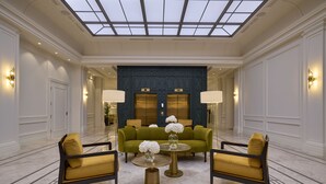 A lobby with a high ceiling, a central green sofa, two yellow armchairs, a round table with a vase of flowers, and a glass ceiling. - Hotel Saski Krakow, Curio Collection by Hilton (Kraków)