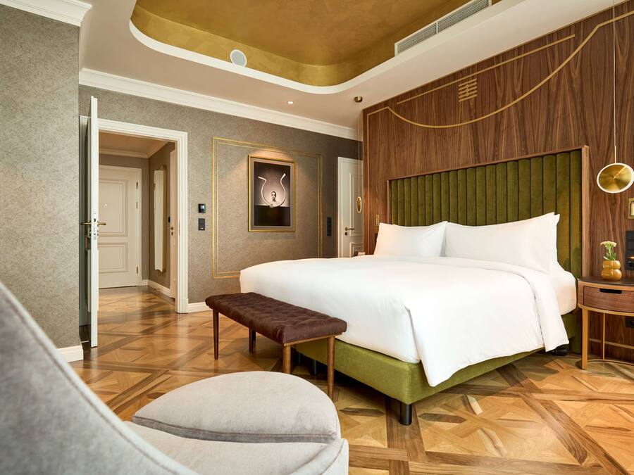 Una habitación de hotel moderna con una cama grande, un banco y una pequeña mesa con un florero.