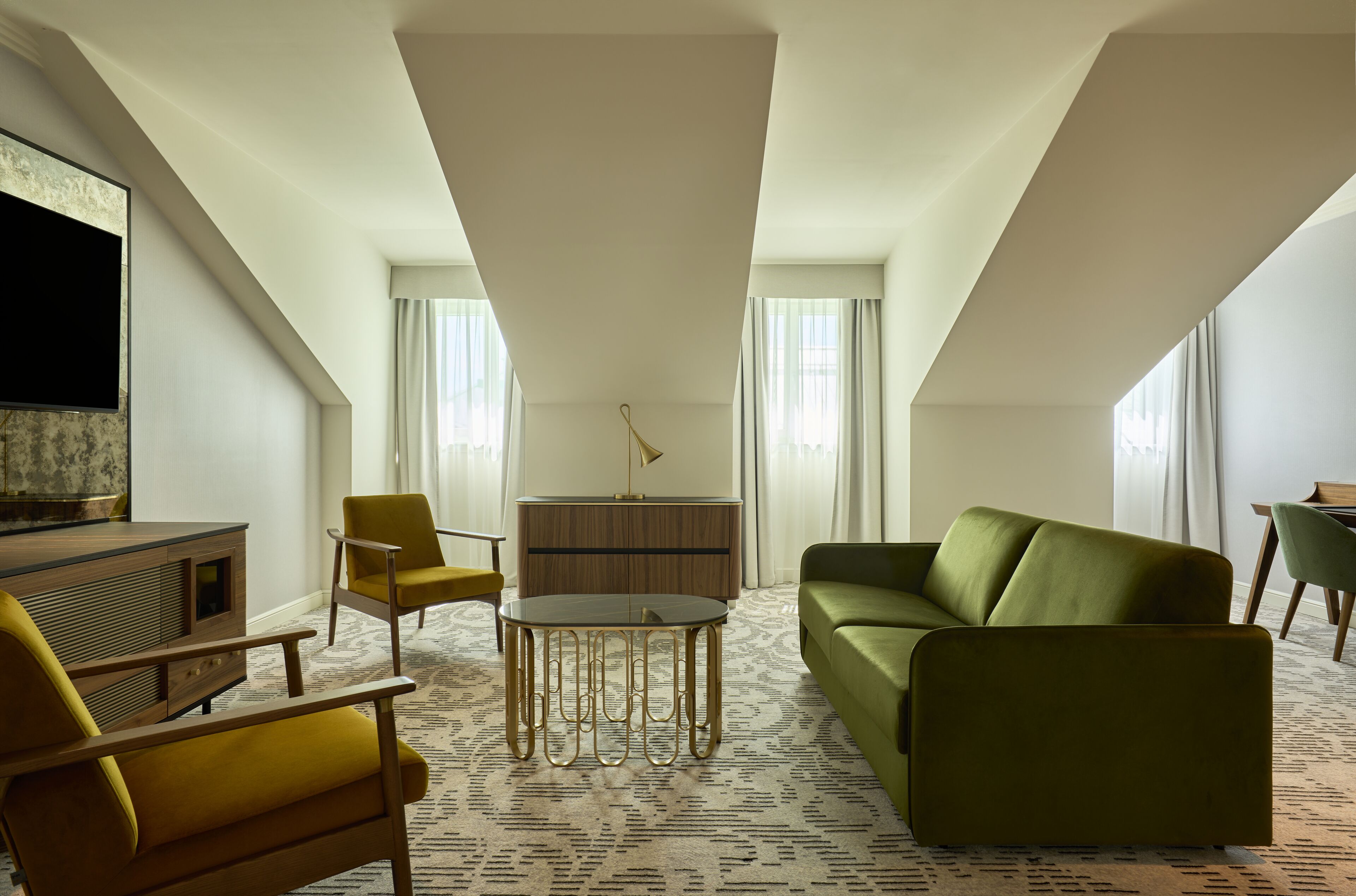 A modern hotel room with a green sofa, yellow armchairs, a wooden cabinet, and a flat-screen TV.