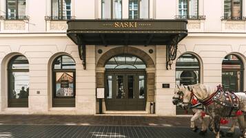 Un edificio con un letrero que dice 'HOTEL SASKI KRAKÓW' sobre la entrada. Hay dos caballos con arneses decorativos frente al edificio.