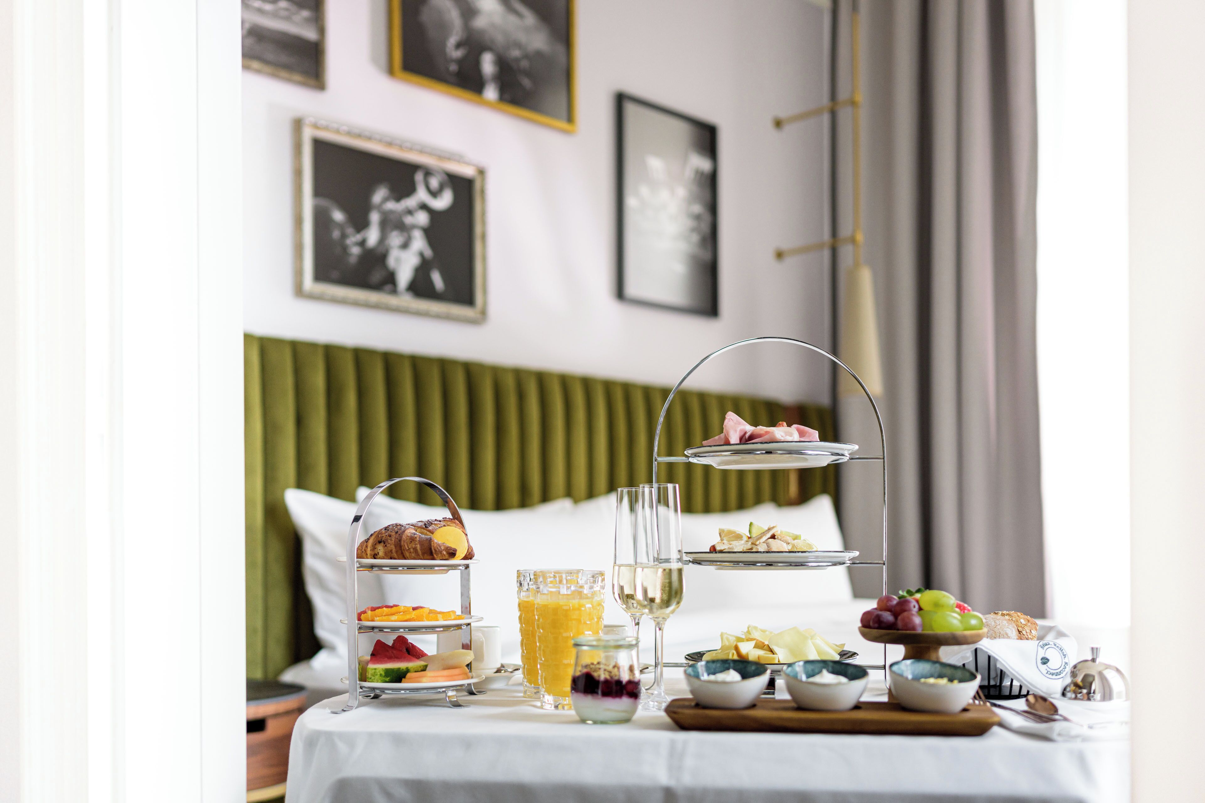 Una mesa en una habitación de hotel con un servicio de desayuno que incluye una bandeja escalonada, un vaso de jugo y diversas frutas y pasteles.
