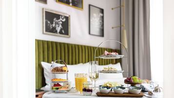 Ontbijt met een etagère, een glas sap en diverse soorten fruit en gebak op een tafel in een hotelkamer.