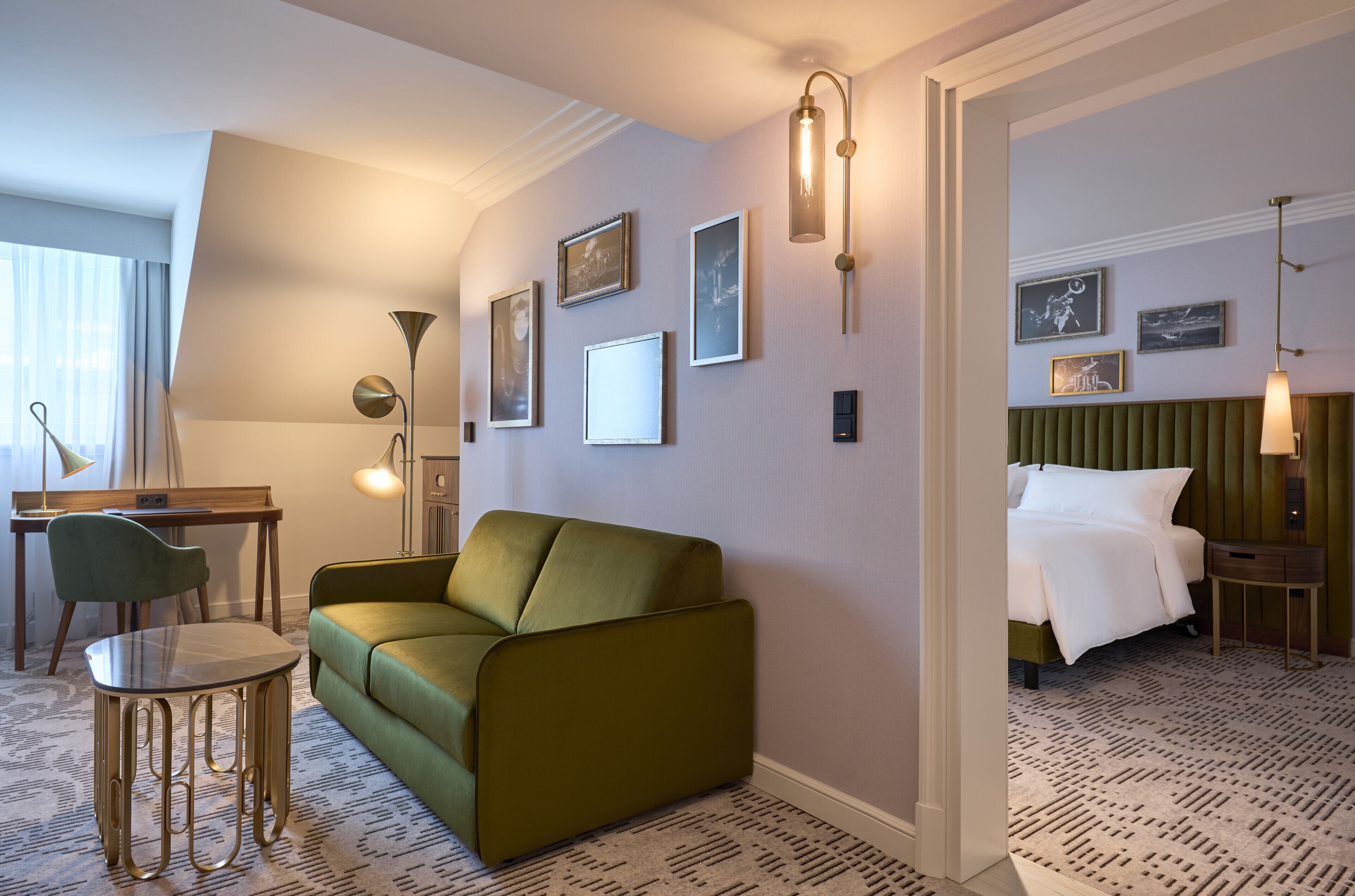 A hotel room with a green sofa, a small table, a desk, and a bed with a green headboard.