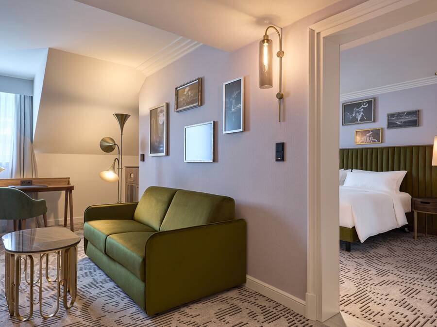 A hotel room with a green sofa, a small table, a desk, and a bed with a green headboard.