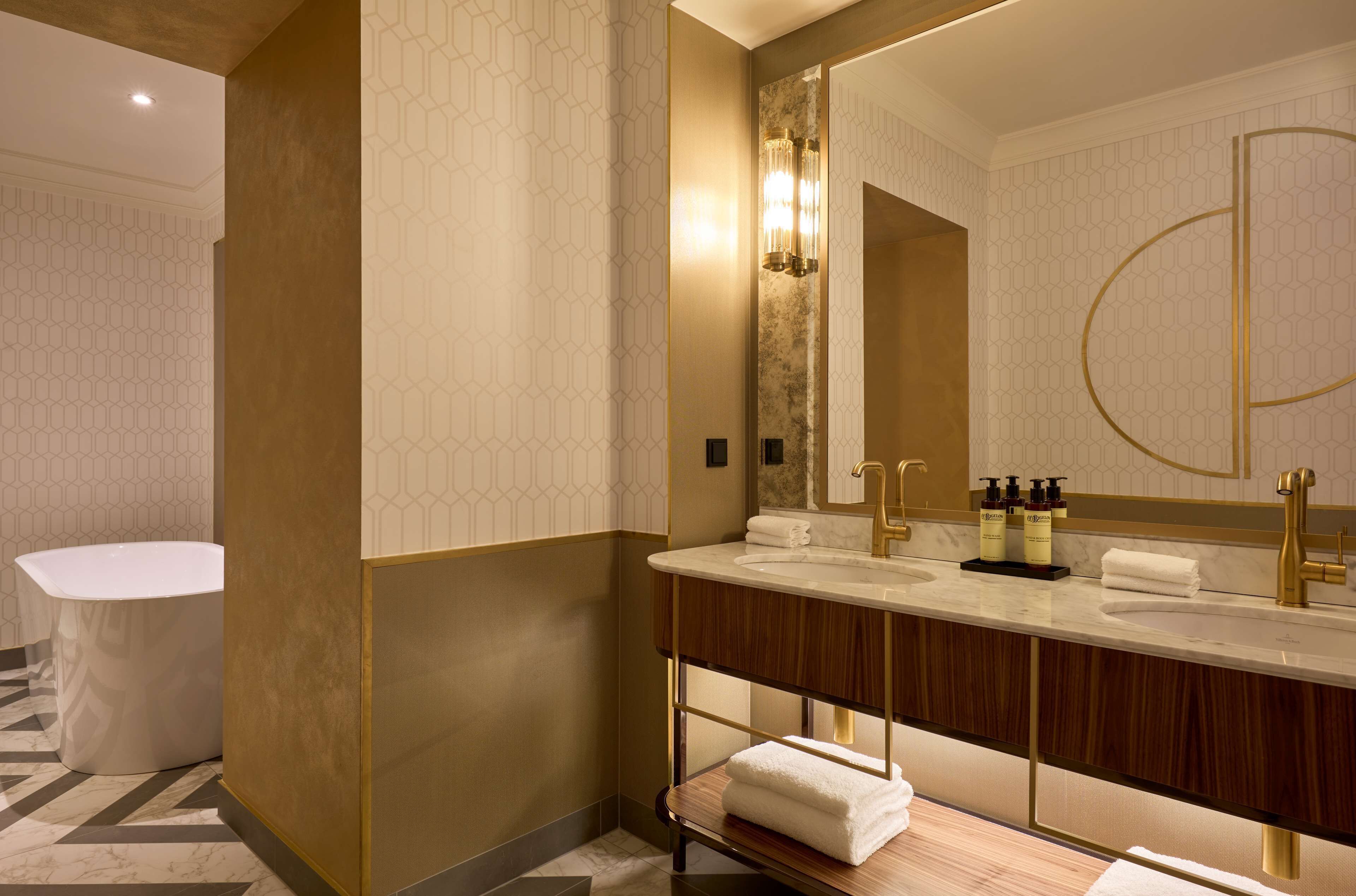 A modern bathroom with a large mirror, dual sinks, and a standalone bathtub.
