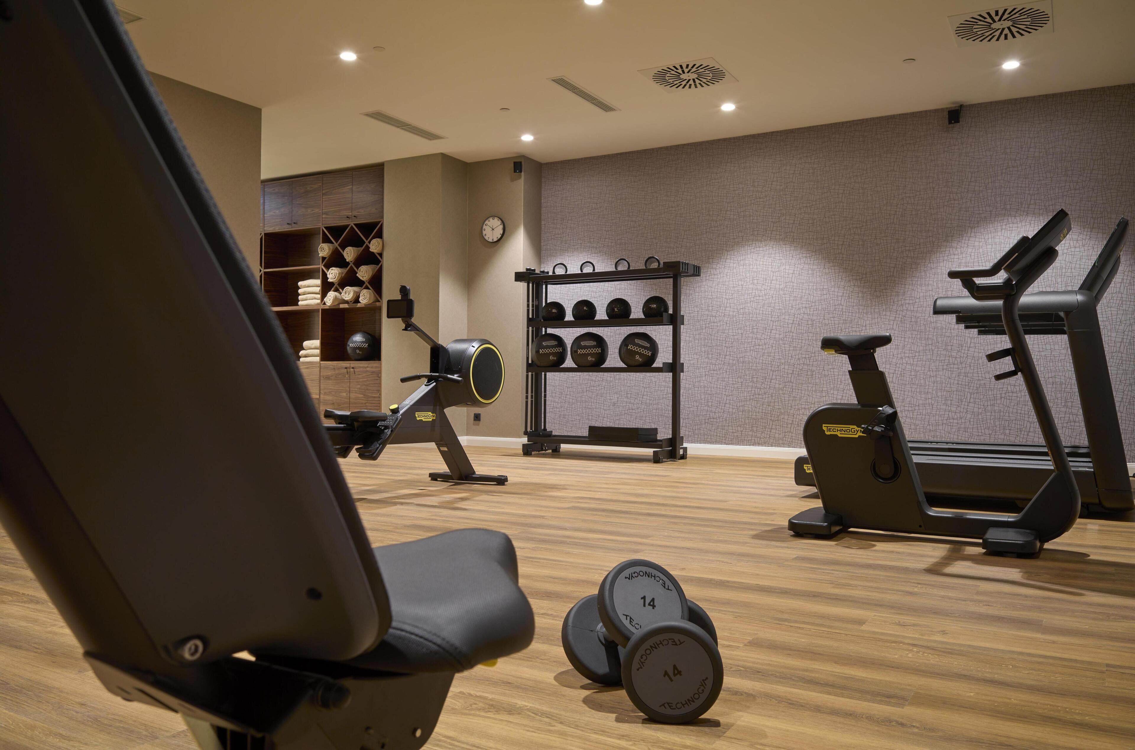 Un gimnasio con equipo de ejercicio, incluyendo pesas, una cinta de correr y estanterías para pesas.
