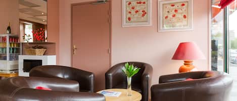 A hotel lobby with leather chairs, a small round table, a vase with flowers, and two framed pictures on the wall.