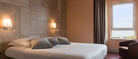 Habitación de hotel con una cama grande, dos lámparas de pared, una ventana con cortinas y una silla.