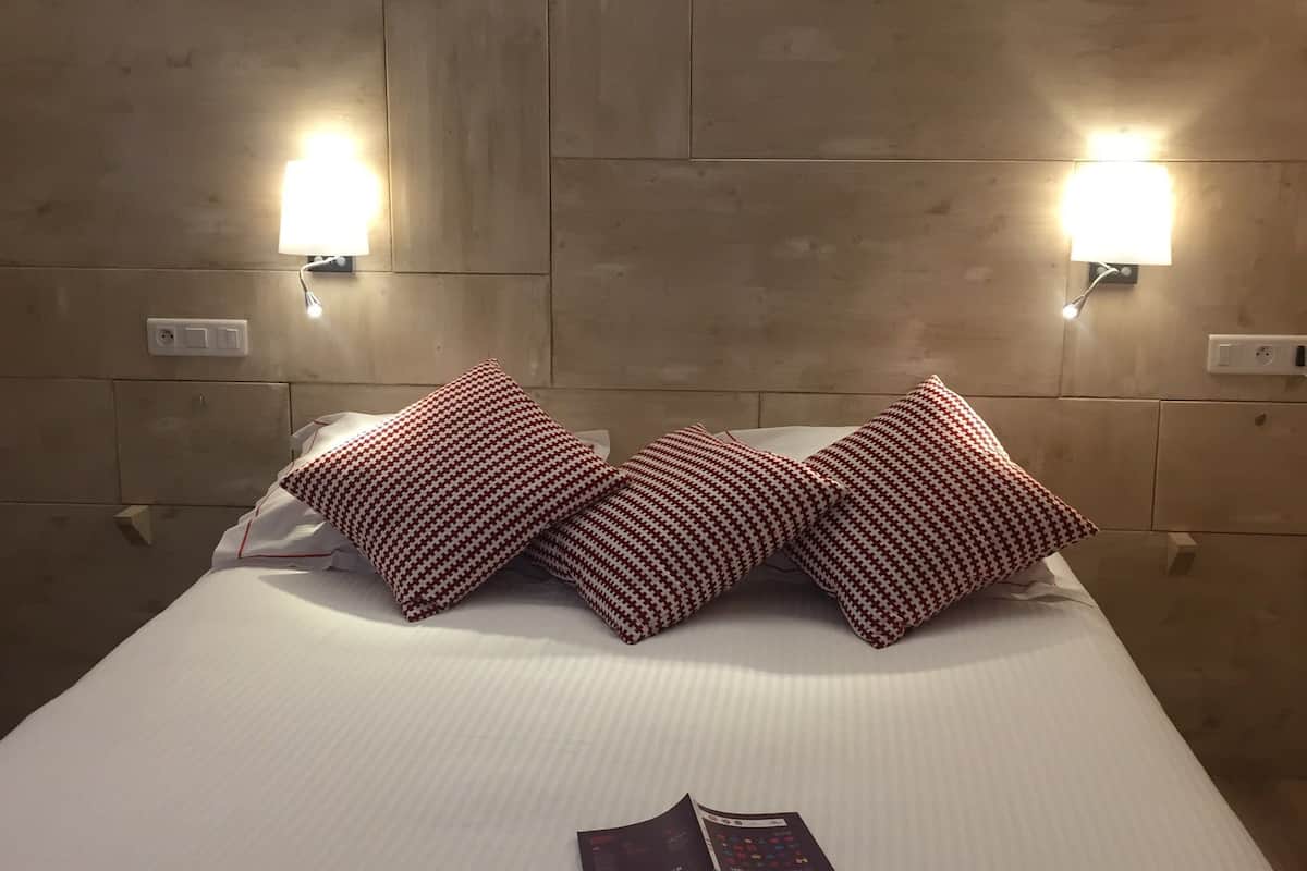 A hotel room with a large bed, two wall-mounted lights, and a checkered pillow.