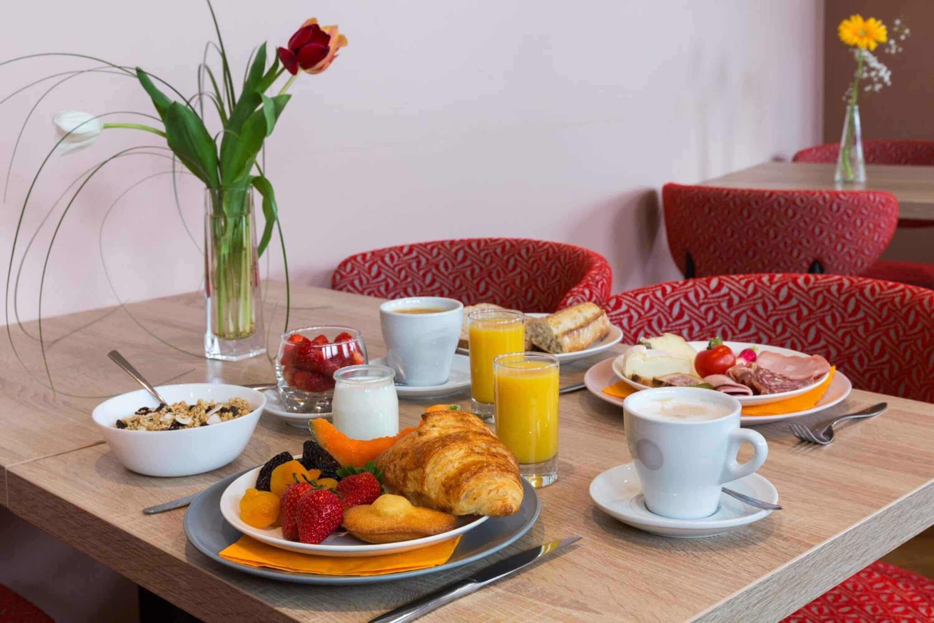 Uma mesa de café da manhã com pratos de comida, um croissant, morangos e um copo de suco de laranja.